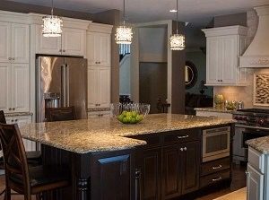 An eye catching kitchen with contrasting cabinets of dark brown cherry and maple cream glaze. Giallo Napoli granite countertops, and subway backsplash tile in polished Crema Marfil, with a glass and stone mosaic framed accent over the stove add to the kitchen’s elegance. The stunning Schonbek island pendant lights complete this lovely space. #newjerseykitchendesign #designnewjersey #newjerseykitchendesigncenter #maplecabinets #twotonedkitchen #designnj #kitchenremodeler