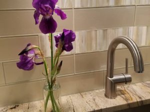 Garden irises in our client’s renovated kitchen!  #glasssubwaytile #undercabinetlighting  #undermountsink #kitchendesign #kitchenandbathrenovation #irises #purpleflowers  #stainlessfaucet #granitecounters